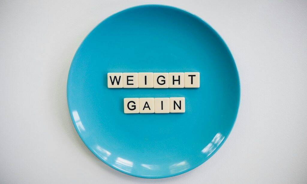 Scrabble tiles spelling 'weight gain' on a blue plate, symbolizing health and diet.
