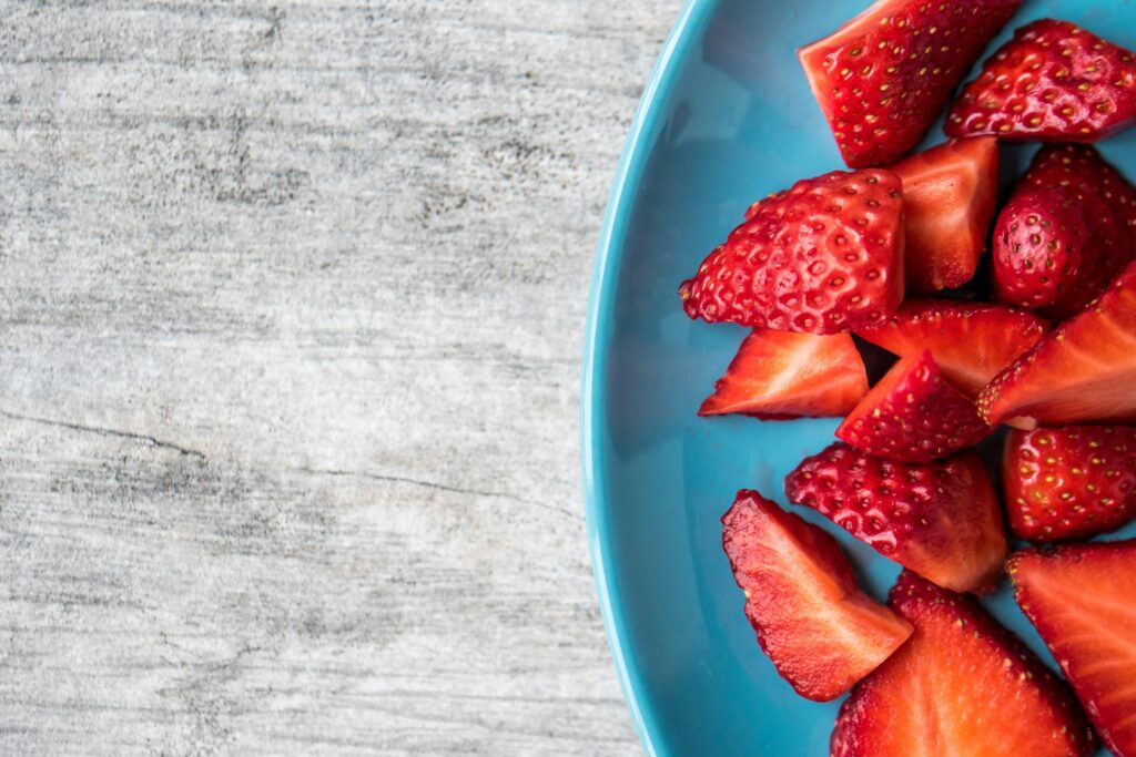 A close-up of fresh organic strawberries sliced on a blue plate for a healthy snack.