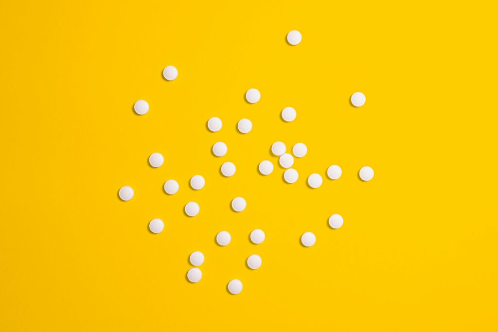 White pills scattered on a vibrant yellow background, symbolizing medical treatment and health care.