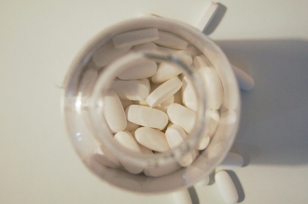 Overhead view of white pills inside a glass jar on a light surface, emphasizing healthcare and medication themes.