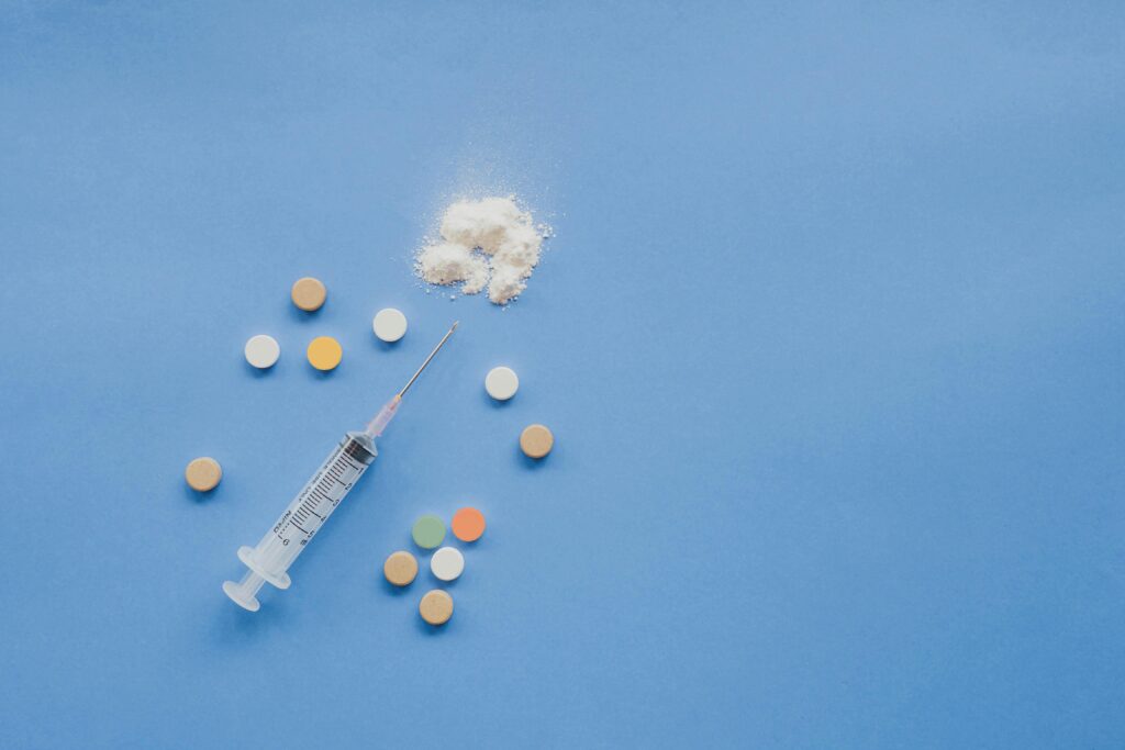 Syringe, pills, and powder arranged on a blue background representing healthcare concepts.
