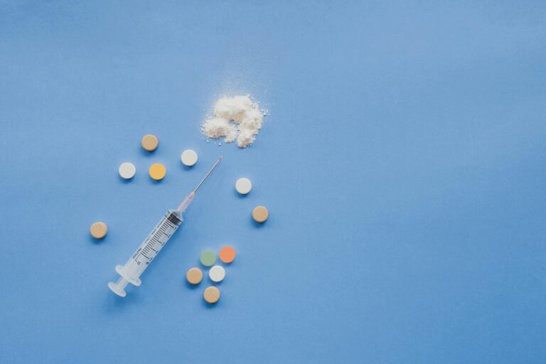 Syringe, pills, and powder arranged on a blue background representing healthcare concepts.